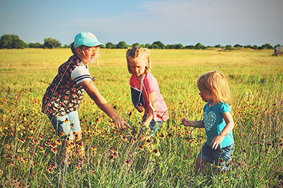 Three young girls ages three, five, and eight picking yellow wildflowers in Lake Dewberry RV Resort's open field in the glow of the warm evening sun