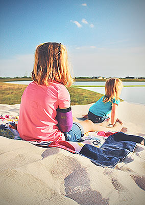 Two young girls sitting on Lake Dewberry RV Resort's sand beach watching the sunset together over the lake.