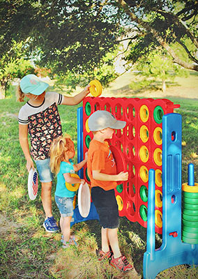 Three young children play a game of giant connect four under the shade of an oak tree.