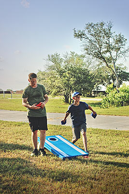 Two teenage boys wearing tshirts and shorts playing a game of cornhole together on Lake Deweberry RV Resort's green, grassy lawn on a warm summer day