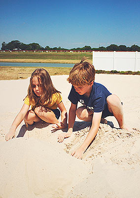 A little boy and girl playing and digging in the sand together at Lake Dewberry RV Resort's fenced-in sand beach by the lake on a sunny summer day