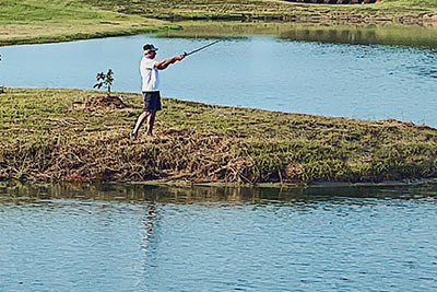 Man standing on the grassy bank of Lake Dewberry RV Resort fishing in the lake