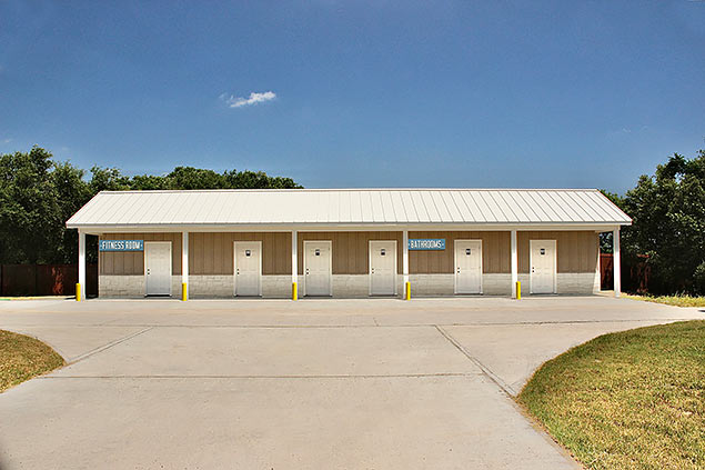 Lake Dewberry RV Resort's 1-story bathroom building with beige walls and a white roof. Signs on the building read: Bathrooms and Fitness Room