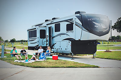 A family consisting of a Mother, a Father, a Grandfather and three children relaxing in the shade with an ice chest on the lawn next to their RV at Lake Dewberry RV Resort
