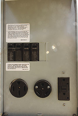 Closeup view of an open electrical box showing the power options available at each RV site: 3 plugs and circuit breakers for 20, 30, and 50 amp connections, respectively.